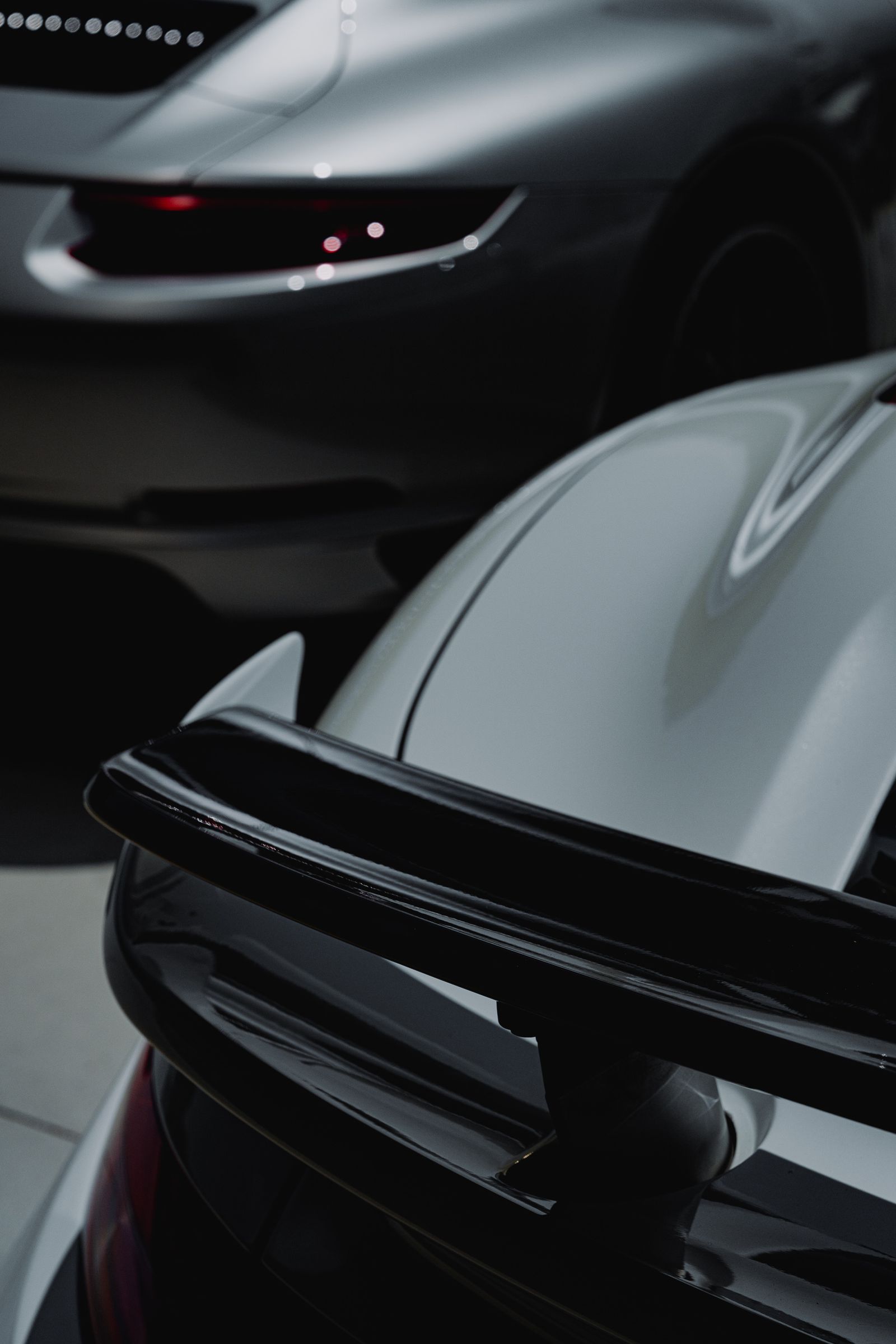 Close-up of the gloss black rear wing and swan-neck mounts of a Porsche 911 GT3 in a dark showroom