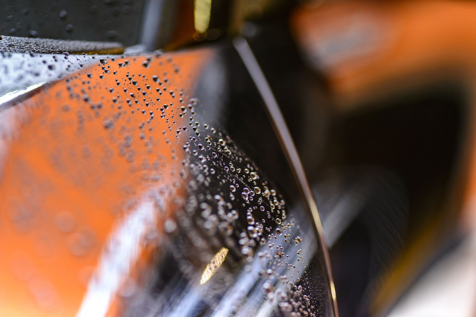 Macro of hydrophobic water beads sitting on a glossy dark car panel with warm orange light reflections
