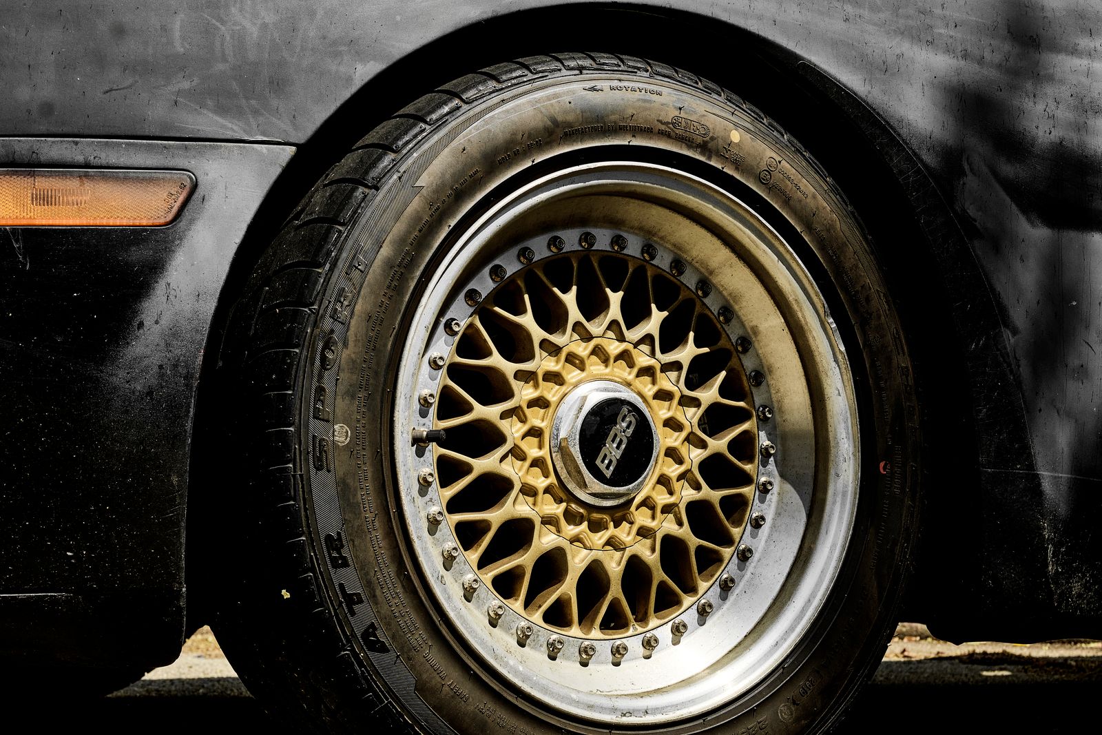 Macro shot of a bronze-gold mesh BBS alloy wheel with polished lip fitted to a black car