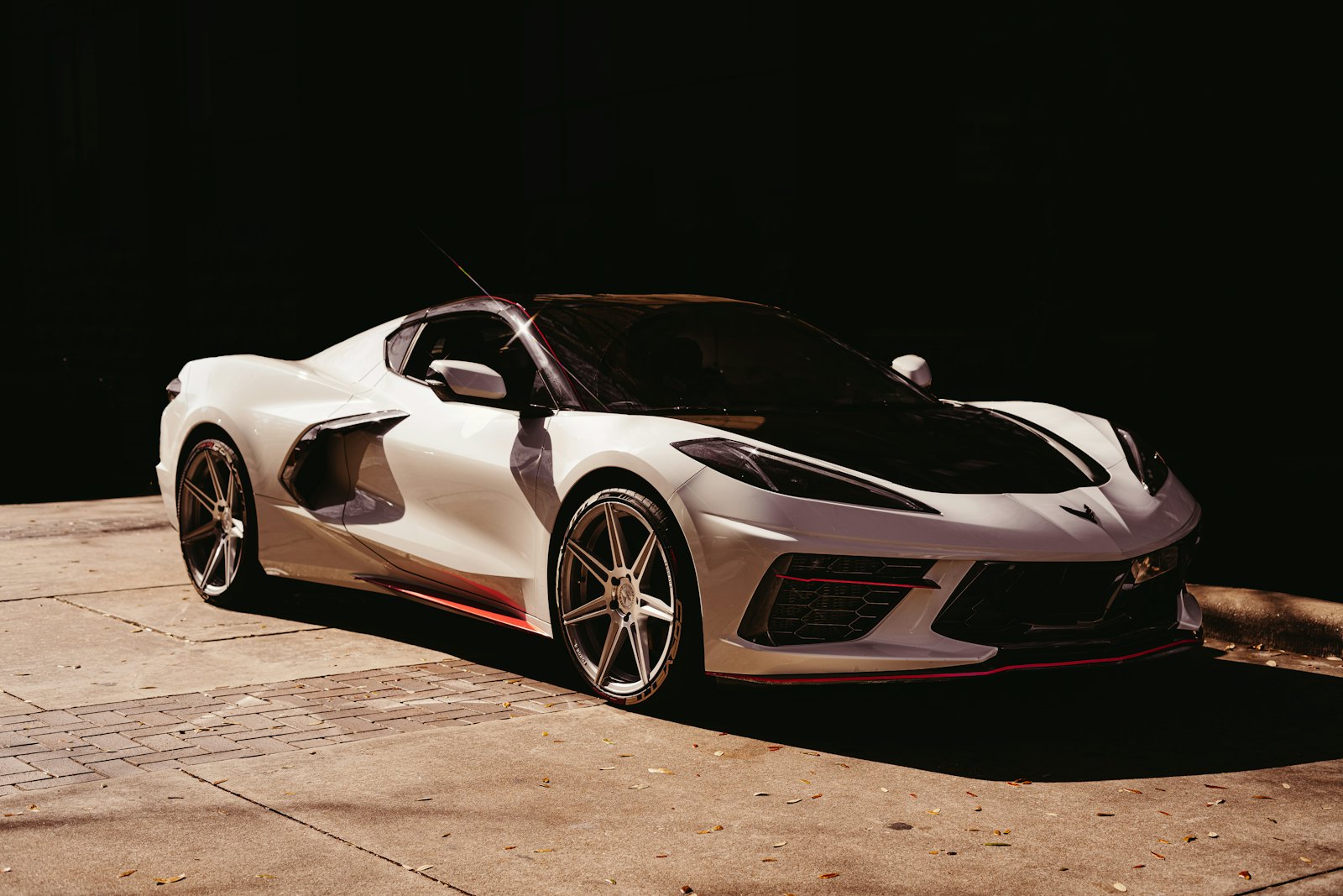 Pearl white mid-engine Chevrolet Corvette C8 lit by a hard shaft of light against a pitch black background