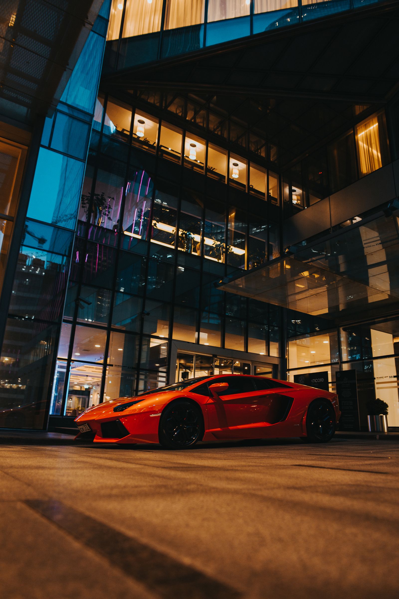 Red Lamborghini Aventador shot from a low angle at night outside a lit glass tower