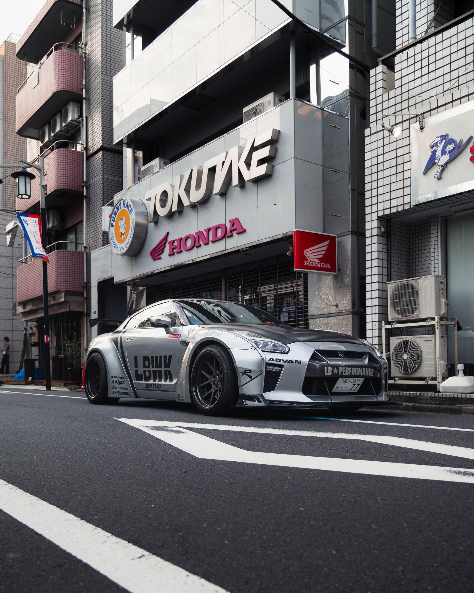 Chrome silver Liberty Walk widebody Nissan GT-R R35 parked on a Tokyo street, shot from a low kerb angle