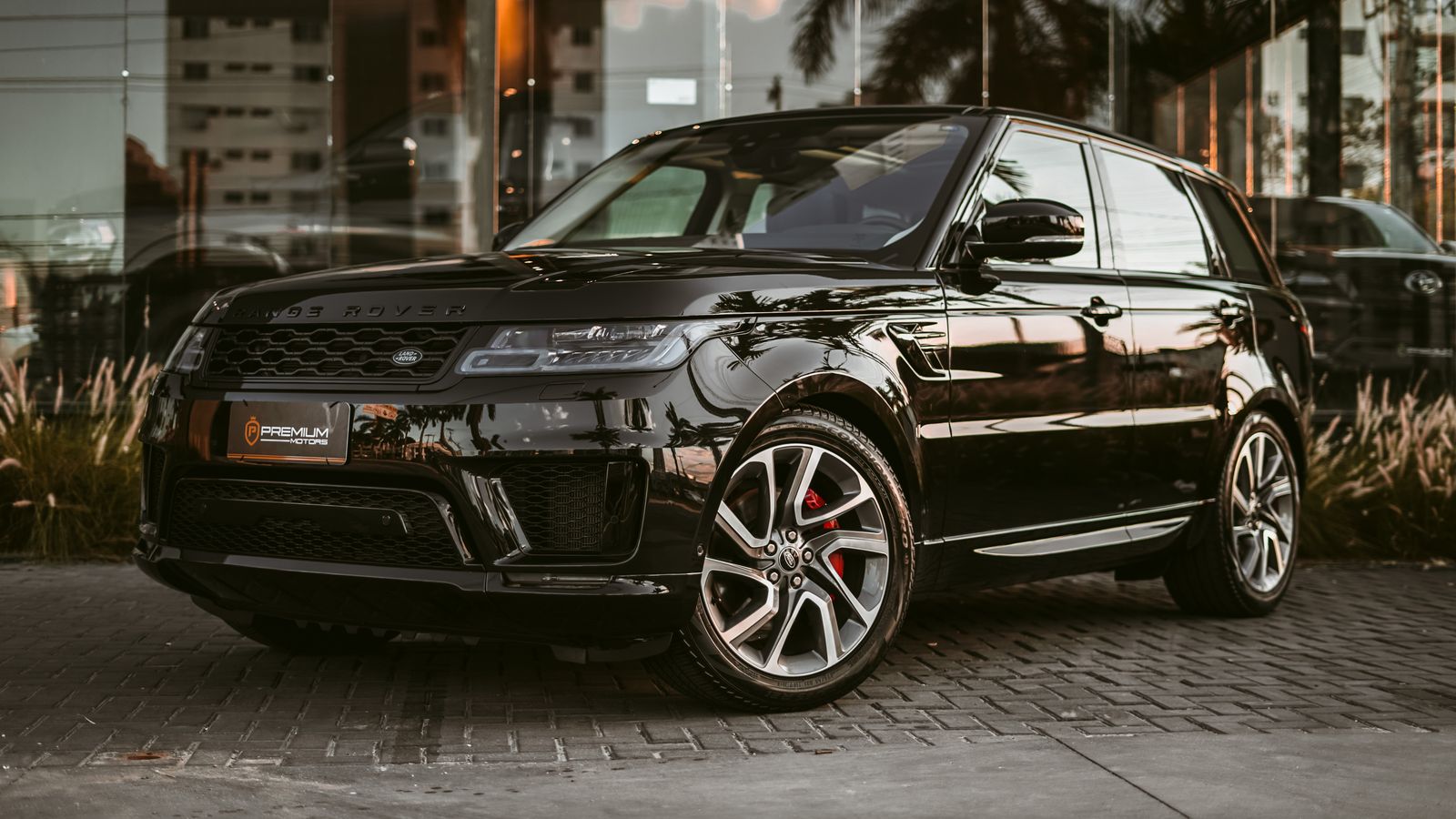 Gloss black Range Rover Sport on stone paving at dusk, palm trees mirrored in the flanks