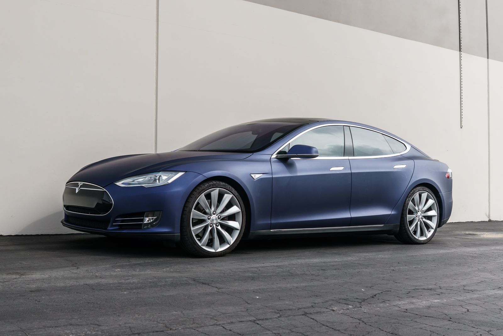 Satin matte blue Tesla Model S in profile against a plain concrete wall, showing a flawless wrap finish